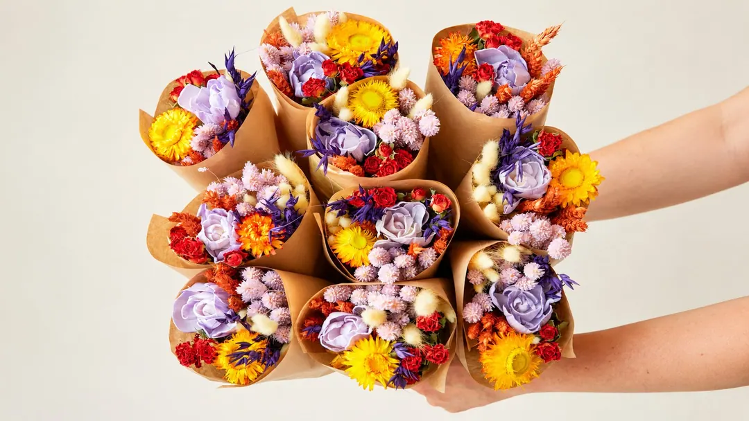 Hands holding a bundle of colorful Dutch dried flower bouquets wrapped in kraft paper